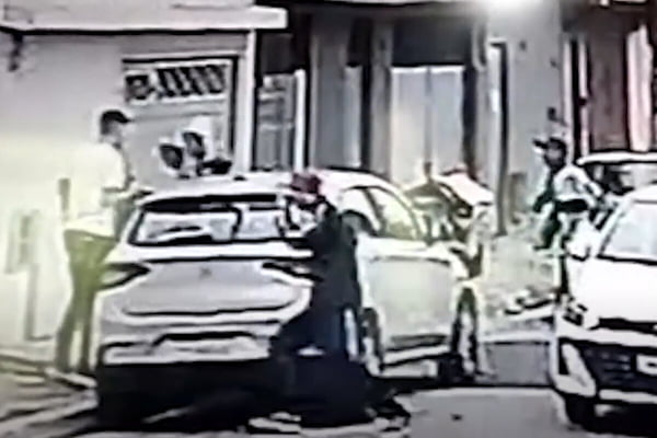 Imagem colorida de ladrões correndo ao lado de carro cinza, em uma rua - Metrópoles