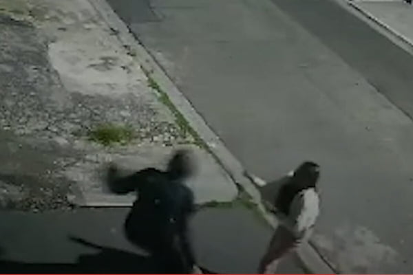 Foto colorida de homem puxando bolsa da mão de mulher no período noturno em rua - Metrópoles