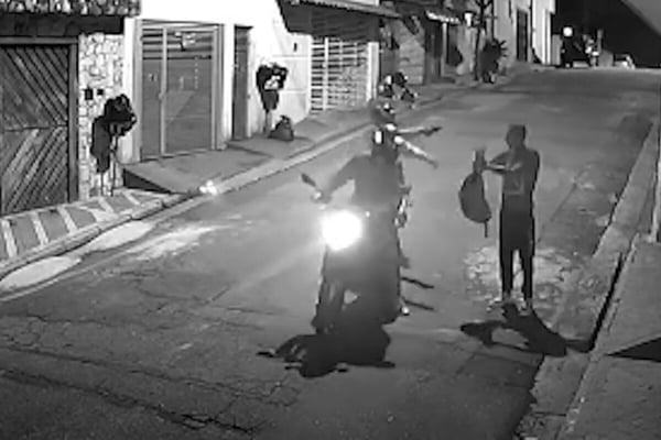 Imagem preto e branco de garupa apontando arma para rapaz segurando mochila - Metrópoles