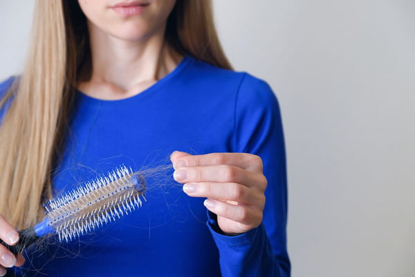 mulher segurando uma escova de cabelo cheia de fios quebrados