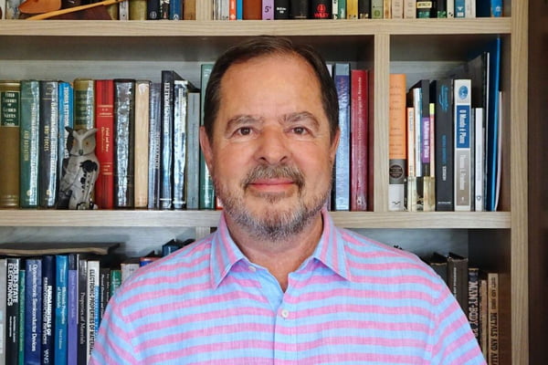 Imagem colorida mostra Sergio Machado Rezende, um homem branco, com barba e bigode grisalhos, vestindo uma camisa polo listrada em azul e rosa na frente de um estante cheia de livros - Metrópoles