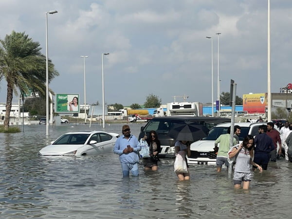 Foto colorida de pessoas percorrem ruas submersas em áreas inundadas enquanto fortes chuvas afetam negativamente a vida cotidiana em Dubai - Metrópoles