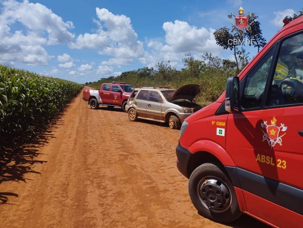 Foto colorida de estrada de terra em meio a plantação com três veículos