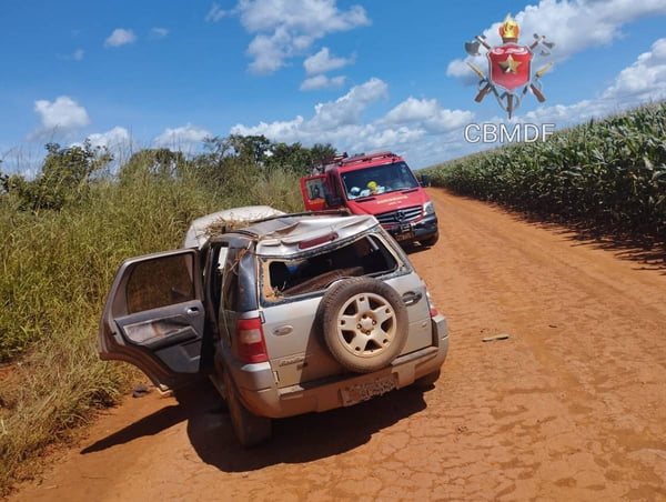 Foto colorida de estrada de terra em meio a plantação com três veículos