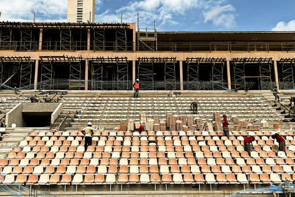 Cadeiras de arquibancada sendo instaladas por homens em estádio