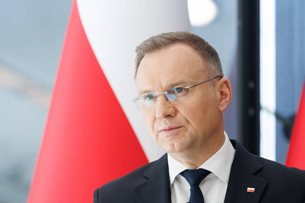 Imagem colorida mostra presidente da Polônia, Andrzej Duda, em frente a bandeira polonesa