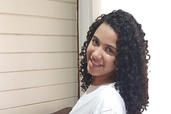 Imagem colorida de menina com cabelo cacheado sorrindo. Metrópoles