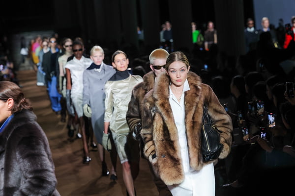 Fila de modelos na passarela da Miu Miu. Gigi Hadid está na frente usando um casaco marrom felpudo - Metrópoles