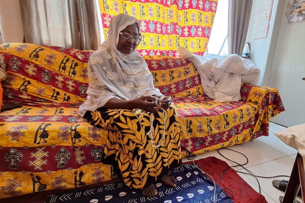 mulher negra de óculos sentada em um sofá com tecidos coloridos