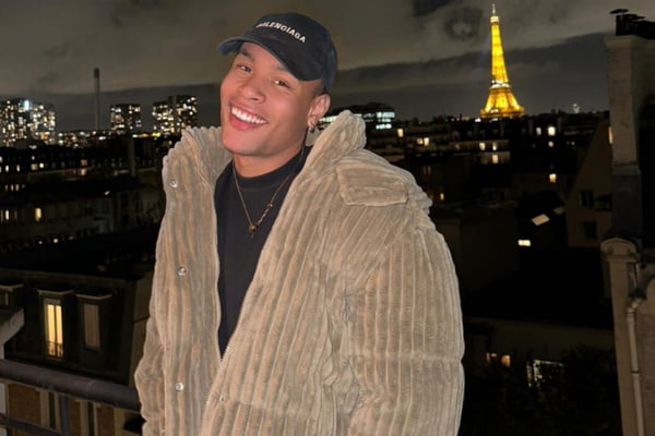 Imagem de homem negro, com casaco e boné, em frente à Torre Eiffel - Metrópoles