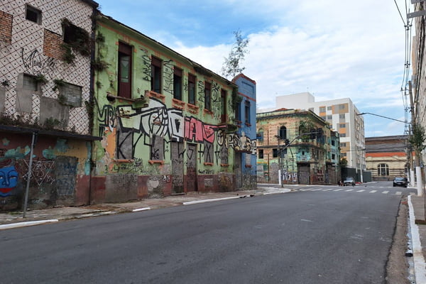 imagem colorida mostra rua vazia, com imóveis abandonados do lado esquerdo. ao fundo da imagme é possível ver um conjunto habitacional - metrópoles