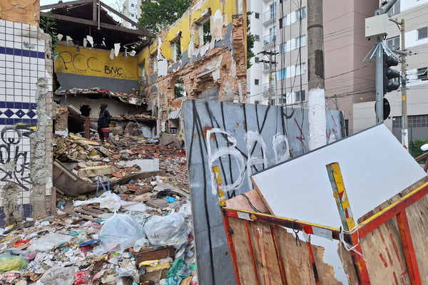 imagem colorida mostra imóvel destruído, com paredes caídas e muito entulho no chão. em uma das paredes, a sigla PCC foi pichada. um homem está no meio da cena com moletom - metrópoles