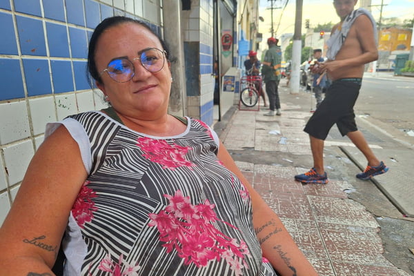 imagem colorida mostra mulher sentada em calçada no centro de são paulo. ela veste uma regata estampada com linhas pretas e flores rosas e usa óculos. metrópoles