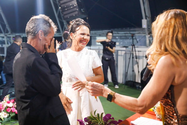 Foto colorida de casal, de casal, homem e mulher, de terno e vestido de noiva, em altar, compartilhando alianças