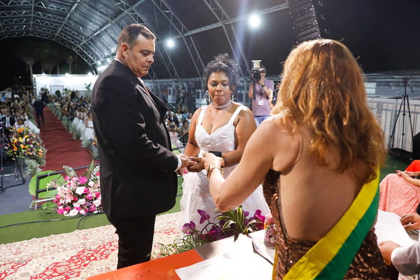 Foto colorida de casal, de casal, homem e mulher, de terno e vestido de noiva, em altar