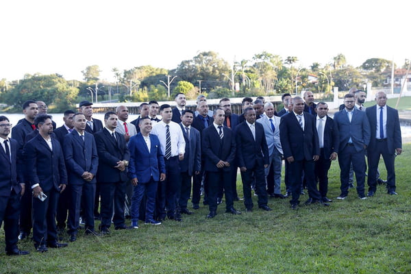 Foto colorida de 50 homens de terno e gravata em pé em gramado