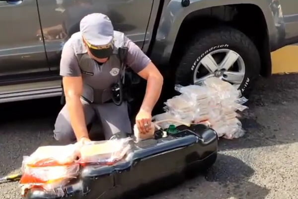 Imagem colorida de PM retirando tijolos de cocaína de tanque de combustível - Metrópoles