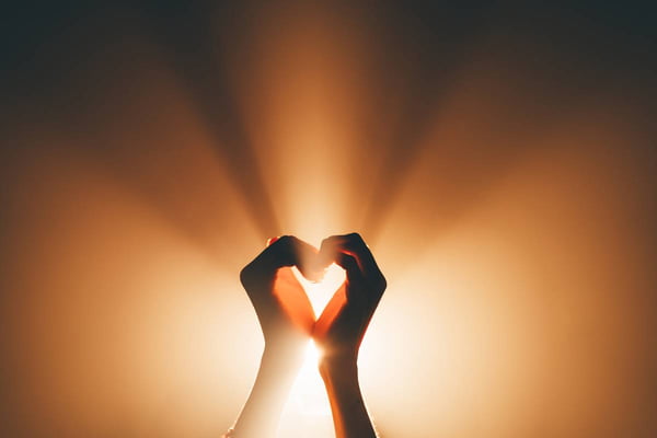 Foto colorida de duas mãos formando um coração contra a luz - Metrópoles
