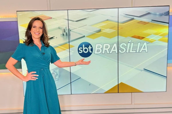 foto colorida de mulher com cabelos curtos iluminados sorrindo e mostrando telão escrito sbt brasília - metrópoles