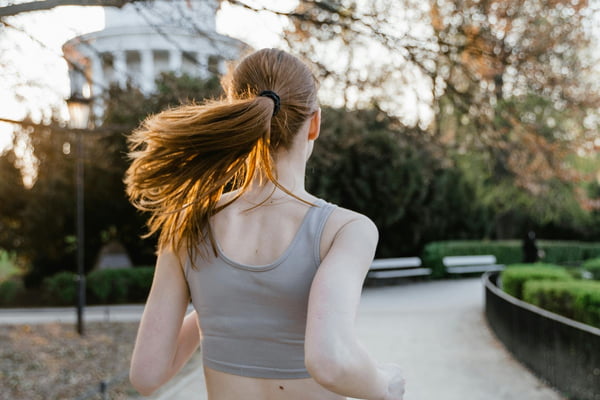 Jovem mulher com cabelo comprido de costas para a foto correndo em parque - Metrópoles