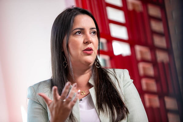 Foto colorida de secretária em entrevista. Mulher branca de cabelos longos e lisos