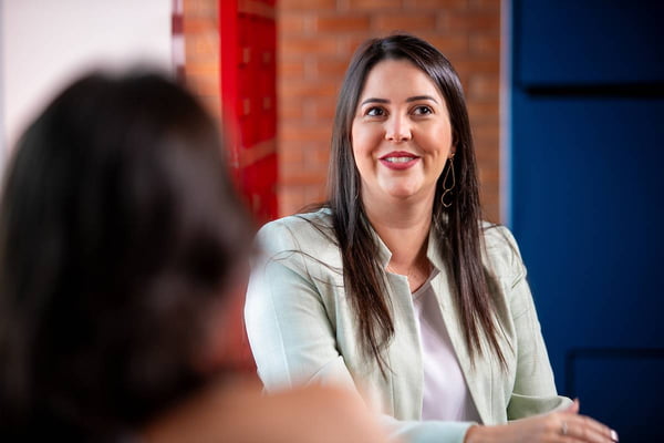 Foto colorida de secretária em entrevista. Mulher branca de cabelos longos e lisos