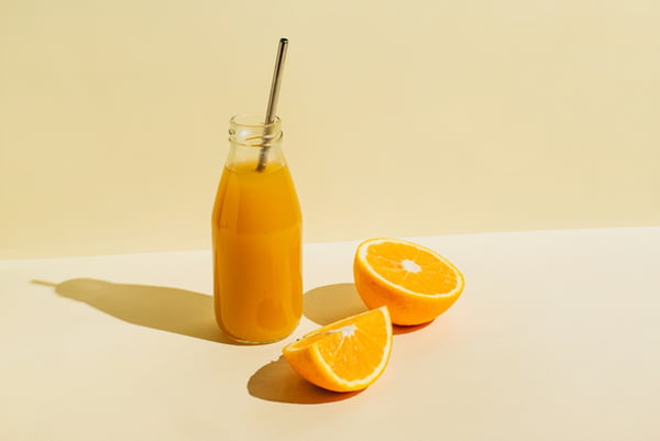 Garrafa com suco de laranja ao lado de uma laranja cortada - Metrópoles