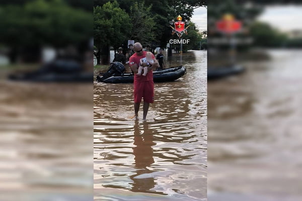 Foto colorida de bombeiro resgatando bebe em rua alagada