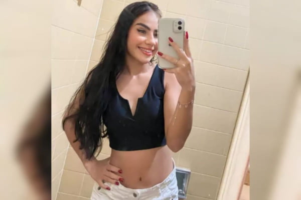 Garota jovem com cabelo e blusa pretos segura celular com um mo - Metrpoles