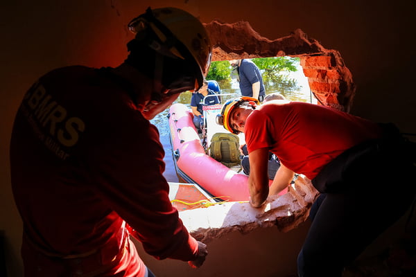 Corpo de Bombeiros abre paredes para acessar pavimento submerso pela água no bairro Mathias Velho em Canoas
