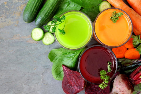 Foto colorida de copos com sucos e legumes cortados e inteiros - Metrópoles