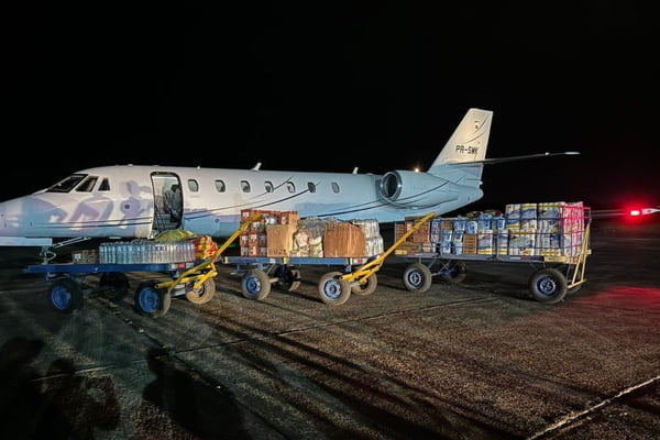 Imagem mostra avião de pequeno porte no solo com caixas de alimentos à frente