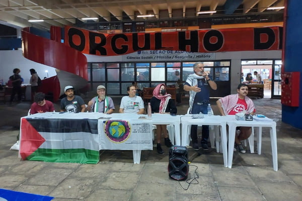 Pessoas sentadas em uma mesa com a bandeira da palestina