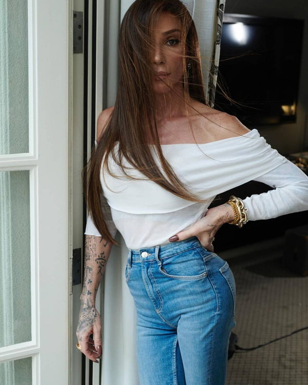 foto colorida de mulher trans de blusa branca e calça jeans - metrópoles