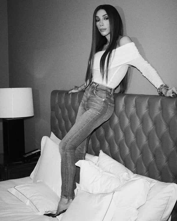 foto em preto e branco de mulher trans em cima de cama de jeans e blusa branca - metrópoles
