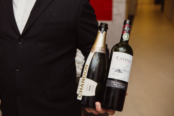 Fotografia colorida mostrando garçom segurando garrafas de vinho e de champanhe-Metrópoles