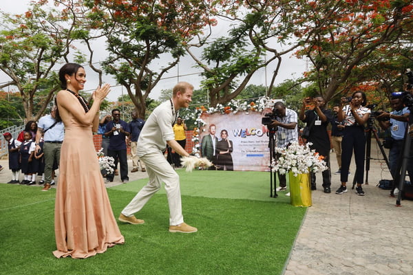 Foto colorida de mulher com vestido coral e homem com roupa clara. Eles estão em um jardim e rodeados por fotógrafos - Metrópoles