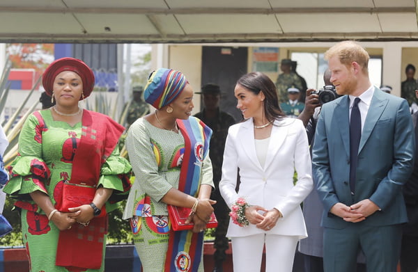 Foto colorida de duas mulheres com roupas coloridas. Uma delas conversa com mulher com terno branco e com homem ruivo - Metrópoles