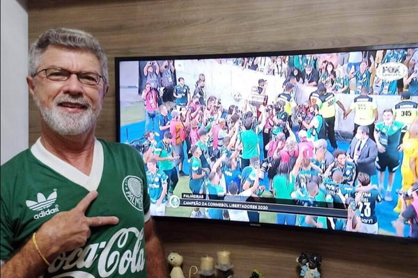 Homem branco, de cavanhaque e cabelos brancos, com camiseta retrô do Palmeiras, em frente à TV ligada transmitindo partida de futebol - Metrópoles