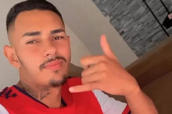 Rapaz pardo, de camiseta vermelha e branca, cavanhaque, fazendo hang lose com a mão esquerda - Metrópoles