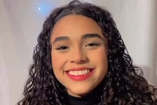 Imagem colorida de menina de cabelos cacheados sorrindo. Metrópoles