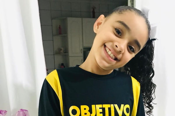 Imagem colorida de menina posando para foto. Metrópoles