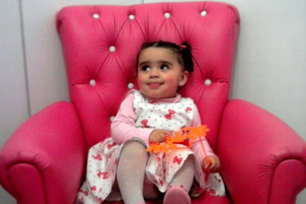 Imagem colorida de uma bebê sentada em uma poltrona rosa. Metrópoles