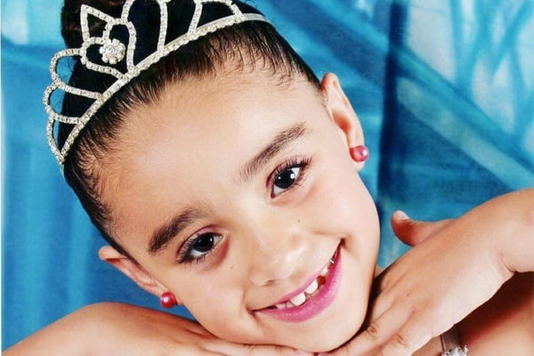 Imagem colorida de menina sorrindo com uma coroa na cabeça. Metrópoles