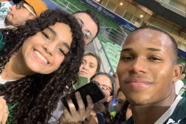Imagem colorida de uma menina tirando foto com um jogador. Metrópoles