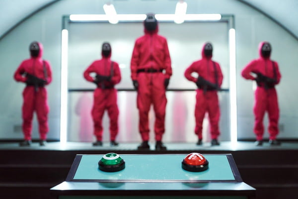 Foto de cinco pessoas de macacão vermelho armadas olhando para botões - Metrópoles