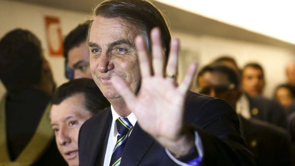 O presidente Bolsonaro em evento, cercado de apoiadores, sorri e cumprimenta-os acenando - Metrópoles