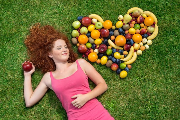 imagem colorida de mulher ruiva deitada em grama com coração de comida ao lado - Metrópoles