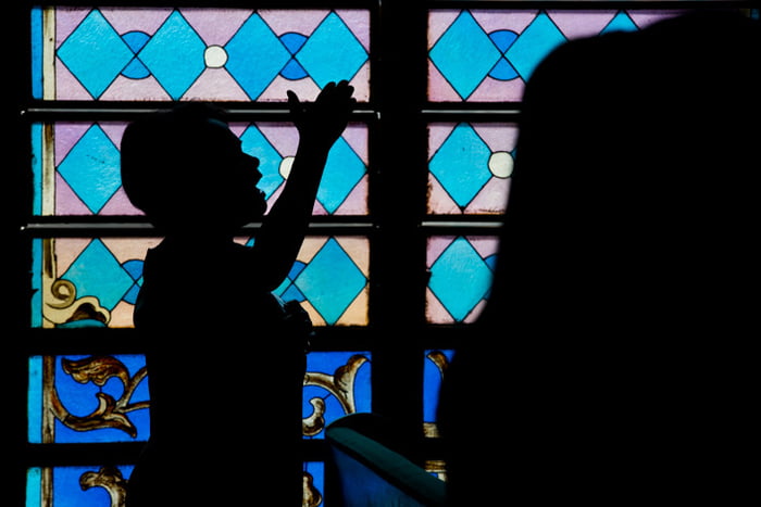 Imagem colorida mostra silhueta de pessoa em culto dentro de igreja - Metrópoles
