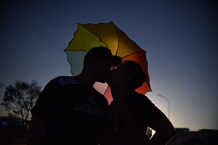Silhueta de dois homens se beijando com guarda-chuva colorido em cima